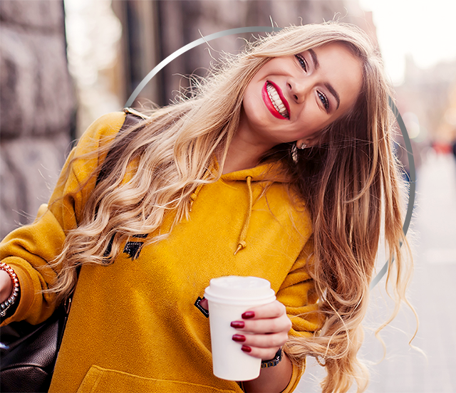 Šťastná mladá žena ve žluté mikině drží papírový kelímek na kávu